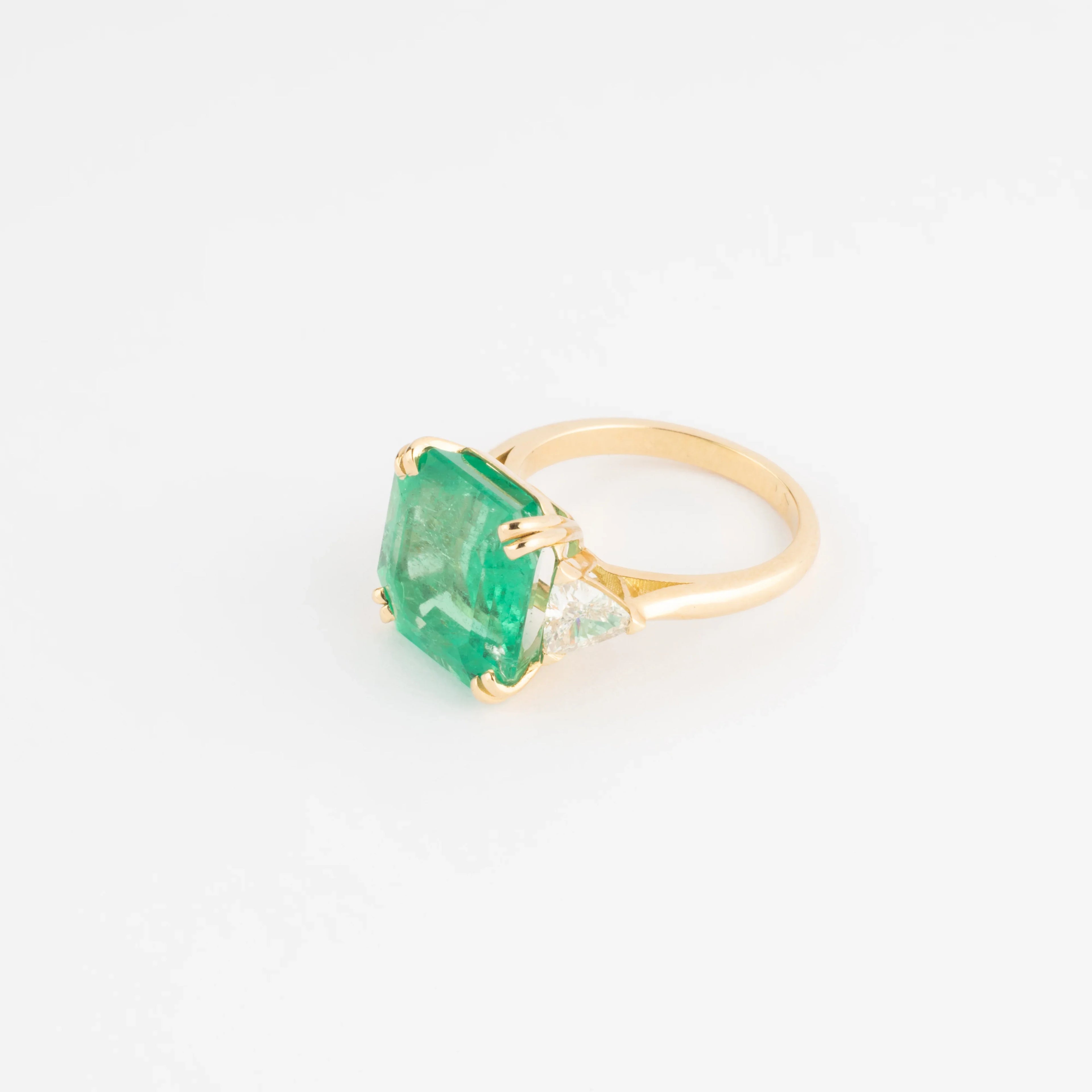 Yellow gold ring adorned with an emerald-cut emerald flanked by triangle diamonds