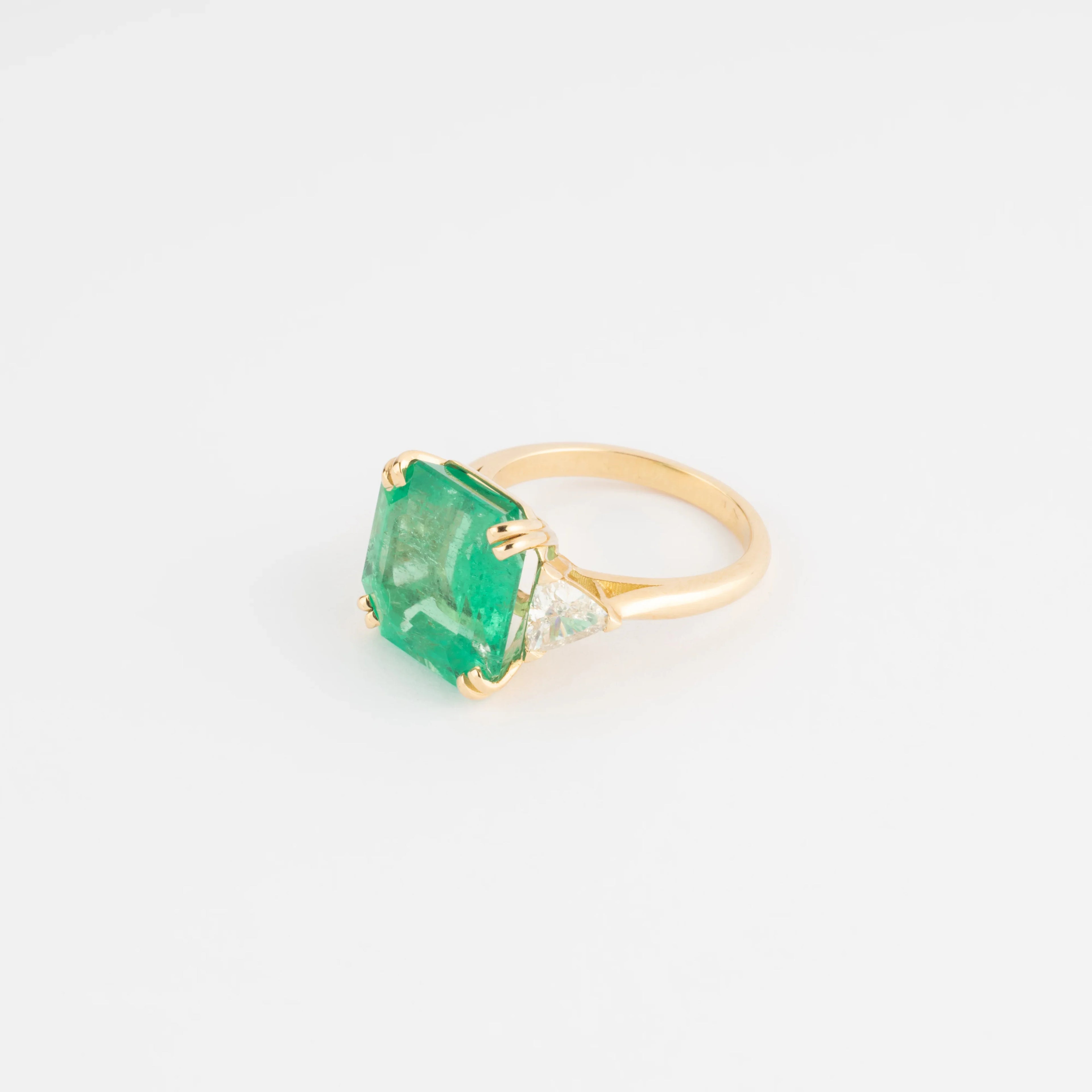 Yellow gold ring adorned with an emerald-cut emerald flanked by triangle diamonds