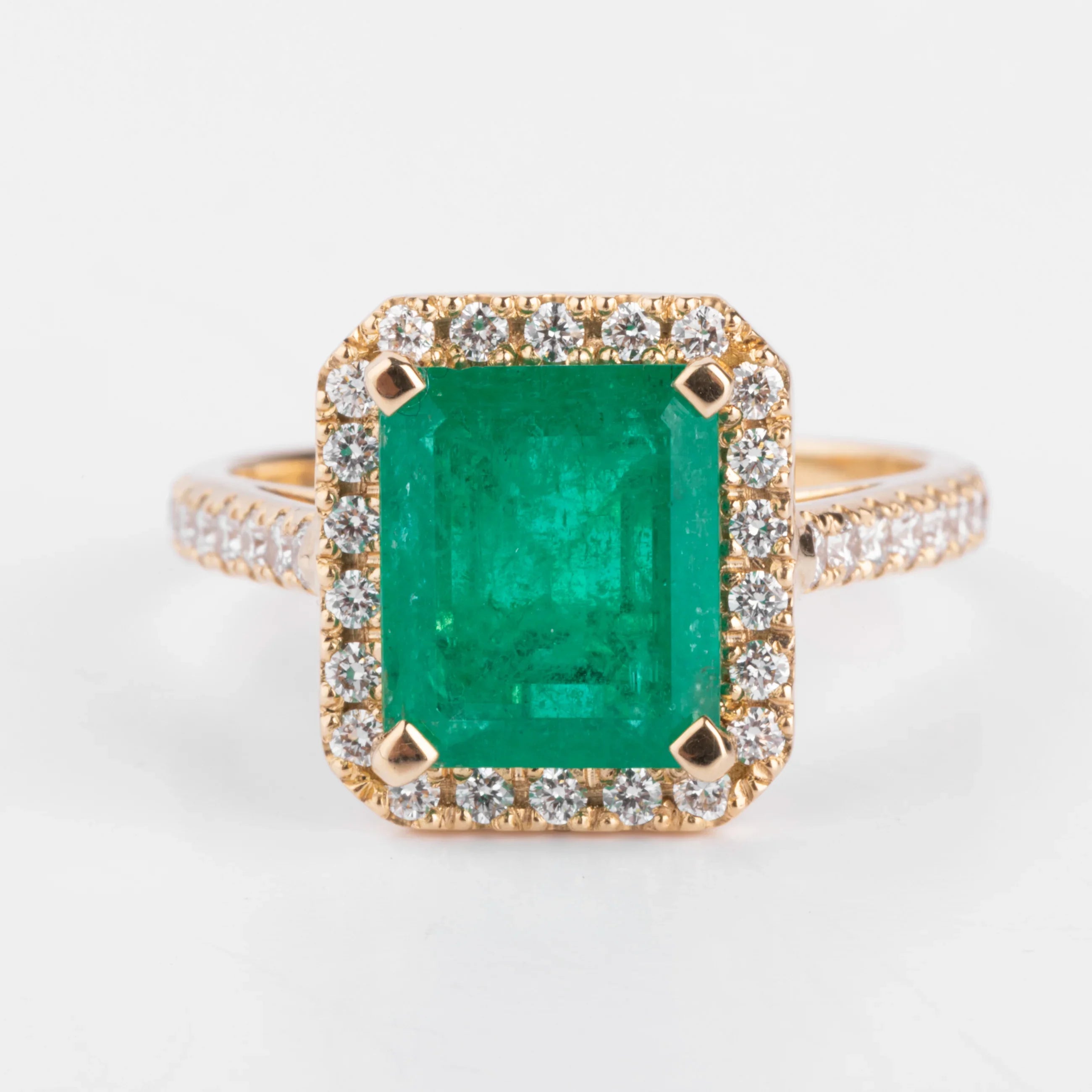 Yellow gold ring adorned with an emerald surrounded by diamonds