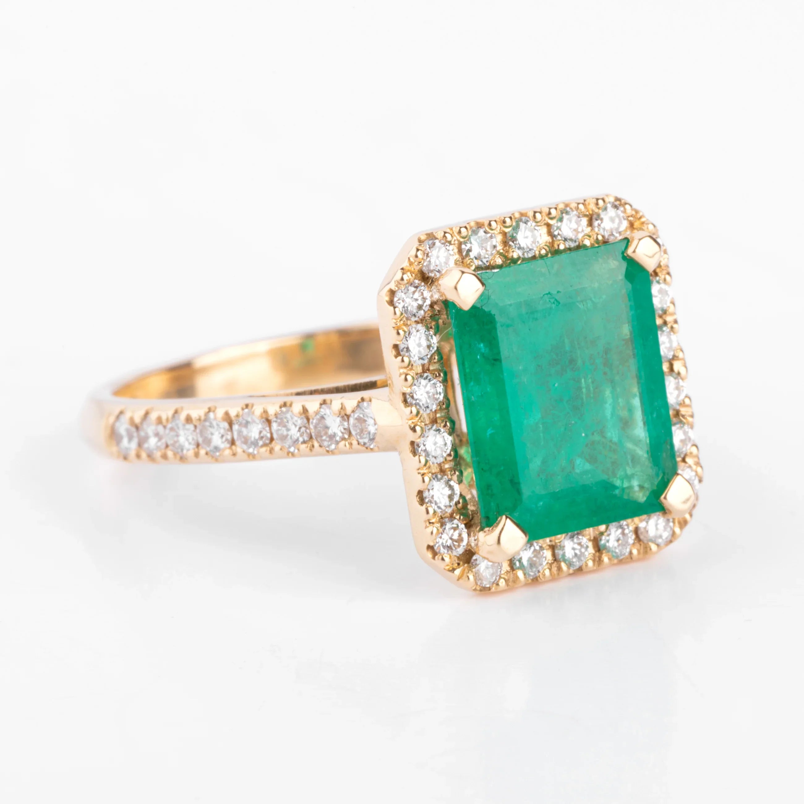 Yellow gold ring adorned with an emerald surrounded by diamonds