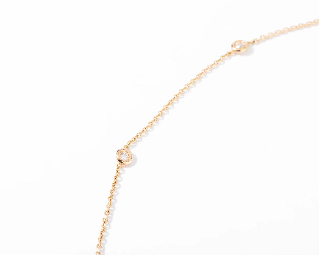 Yellow gold necklace interspersed with 9 diamonds on a cable chain in bezel settings.